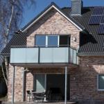 Zweistöckiges Haus mit Balkon, Solaranlage und Terrasse mit Tisch und Stühlen.