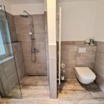 Badezimmer mit Dusche, Toilette und Fliesenboden.