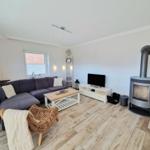 Wohnzimmer mit Sofa, Kaminofen und Holzboden. Fernseher und Couchtisch sichtbar.