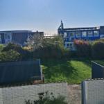 Hinterhof mit grünem Rasen, weißen Mauern und Blick auf blaue Gebäude unter blauem Himmel.