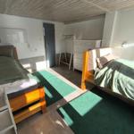 Zwei Betten mit grünen Bettdecken, Schrank und Kleiderständer im Raum.