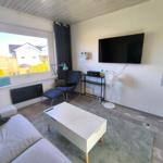 Wohnzimmer mit Sofa, Fernseher und Fensterblick auf Häuser.