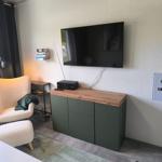 Wohnzimmer mit Fernseher, grünem Schrank und weißem Sessel.