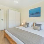 Schlafzimmer mit Bett, Nachttischen und Wandbild. Holzboden und weiße Möbel.