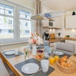 Essbereich mit Tisch, Stühlen und Frühstück. Küchenzeile mit Spüle, Kühlschrank und Kochfeld.