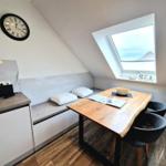 Dachgeschosszimmer mit Schlafcouch, Tisch und Sitzgelegenheit. Fenster zeigt Blick auf Haus.