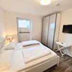 Schlafzimmer mit Doppelbett, Kleiderschrank, TV und Fenster.
