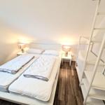 Schlafzimmer mit Doppelbett, zwei Nachttischen und einer Leiter zur Dachgeschosswohnung.