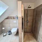 Dusche mit Glaswand, WC und Fenster im Dachbodenbad.