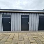 Drei geschlossene Türen mit Beschriftungen an einer Holzwand.