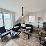 Wohnzimmer mit Sofa, Couchtisch und Schreibtisch. Große Fenster und Holzboden.