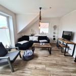 Wohnzimmer mit Sofa, Couchtisch und Fernseher. Holzboden und große Fenster.