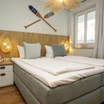 Schlafzimmer mit Bett, Nachttisch und Fenster. Wanddekoration mit Ruder und Lampen.