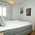Schlafzimmer mit Bett, Fenster, Wandbildern und Deckenleuchte.