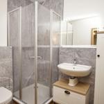 Badezimmer mit Dusche, Waschbecken und Toilette. Wandverkleidung aus grauem Marmor.
