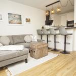 Wohnbereich mit Sofa, Barhocker und Küchenzeile. Holzboden und Wandbilder.
