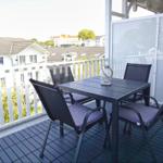Terrasse mit Tisch und vier Stühlen, Blick auf Wohnhäuser und Bäume.