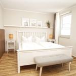 Ein Schlafzimmer mit weißem Bett, Holzboden und Fenstern.