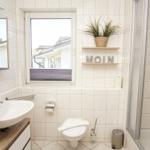 Badezimmer mit Waschbecken, Toilette und Dusche. Fenster mit Blick nach draußen.