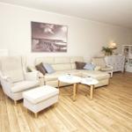Wohnzimmer mit cremefarbenem Sofa, Sessel und Holzboden. Wandbild und Beistelltische.