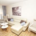 Wohnzimmer mit cremefarbenem Sofa, zwei Sesseln und einem Tisch. An der Wand hängt ein Bild.