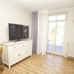Wohnzimmer mit TV-Schrank, Holzboden und Balkontür. An der Wand hängt ein Kranz.