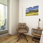 Zimmer mit Bett, Stuhl und Balkonansicht. Wandbild und Nachttisch mit Lampe.