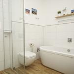 Badezimmer mit Dusche, Toilette und Badewanne. Holzfußboden und weiße Fliesen.