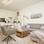 Wohnzimmer mit Sofa, Couchtisch und Küchenbereich. Wandbild mit Strandstühlen.