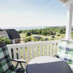 Terrasse mit Tisch und Stühlen, Blick auf Grünflächen und Meer.
