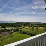 Weitläufiger Blick von Balkon auf Grünflächen, Bäume und Meer unter blauem Himmel.