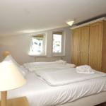 Schlafzimmer mit Doppelbett, Holzschrank und zwei Fenstern.