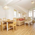 Wohn- und Essbereich mit Sofa, Tisch und Stühlen. Holzfußboden und große Fenster.