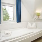 Ein weißes Bett mit Kissen und Handtuch unter einem Fenster mit blauen Vorhängen.