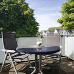 Terrasse mit Tisch und zwei Stühlen. Blick auf grüne Bäume und weiße Häuser.