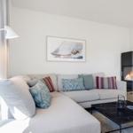 Ein Wohnzimmer mit Sofa, Kamin und Tisch. Wandbild zeigt Segelyacht.