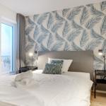 Schlafzimmer mit Bett, Fenster und Palmenwandtapete.