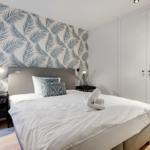 Schlafzimmer mit Bett, Nachttischen und Tapete mit Blättern.