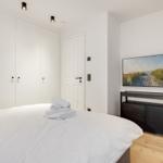 Schlafzimmer mit weißem Bett, Kleiderschrank und Fernseher an der Wand.