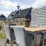 Terrasse mit Holztisch und sechs Stühlen, Blumenkorb, Holz-Zaun und Hintergrundhäuser.