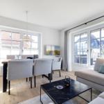 Wohn- und Essbereich mit Sofa, Tisch und Stühlen. Große Fenster und helles Holzfußboden.