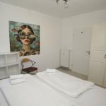 Zimmer mit Doppelbett, Wandbild, Schrank und Stuhl.