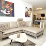 Wohnbereich mit Ecksofa, Couchtisch und Wandbildern. Küche im Hintergrund.