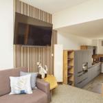 Wohnbereich mit Sofa, TV und Küchenbereich im Hintergrund.