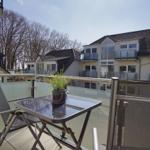 Terrasse mit Tisch, Stühlen und Pflanze. Blick auf moderne Wohnhäuser und Bäume.