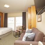 Schlafzimmer mit Bett, Sofa und Balkon. Holzmöbel und Steinwand sichtbar.