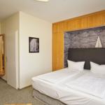 Schlafzimmer mit Doppelbett, Holzmöbel und Steinwand im Hintergrund.