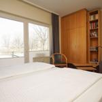 Ein Schlafzimmer mit Doppelbett, Bücherregal und Fenster mit Blick auf Bäume.