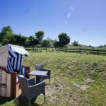 Wilde Strandkörbe und Tische im Garten mit Blick auf grüne Wiesen und Bäume.