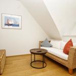 Wohnzimmer mit Sofa, Fernseher und Fenster. Holzboden und schräge Decke.